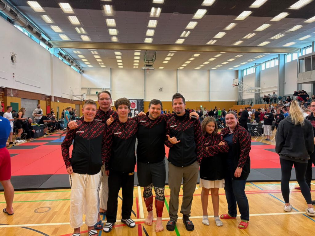 Das Wettkampfteam der Backland Chokers in Vereinsjacken in einer Turnhalle, Erwachsene und Jugendliche nebeneinander